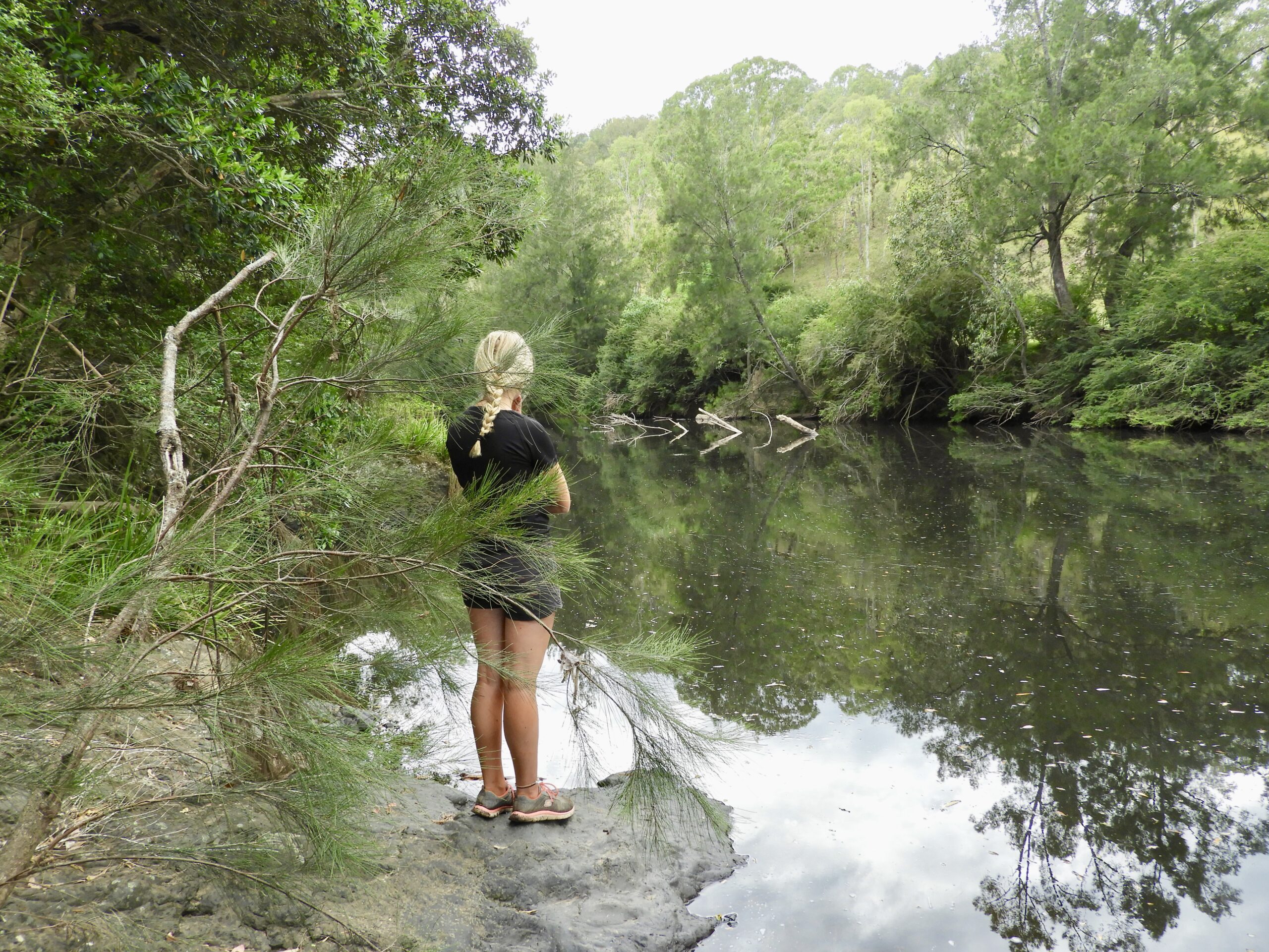 girl with long blond hair in a plait standing on a rock beside a river waiting for the platypus