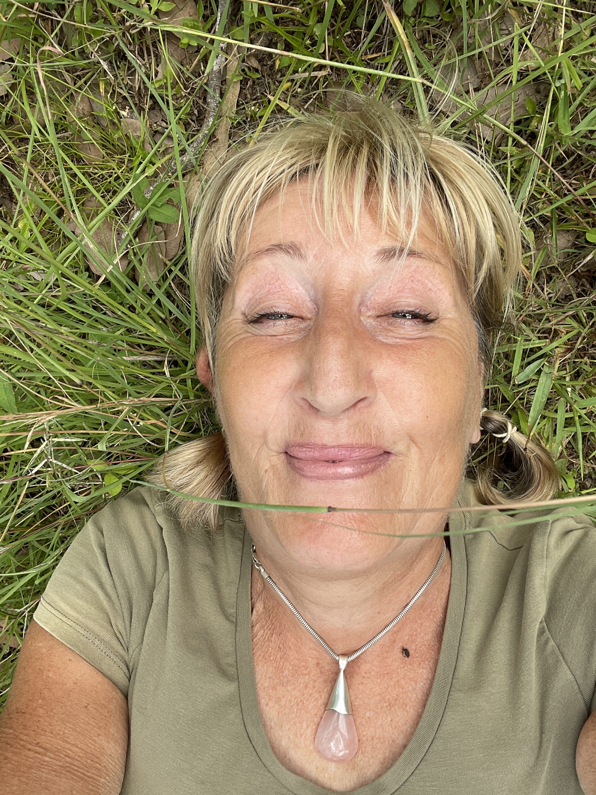 Blonde woman lying on grass with eyes closed and smiling